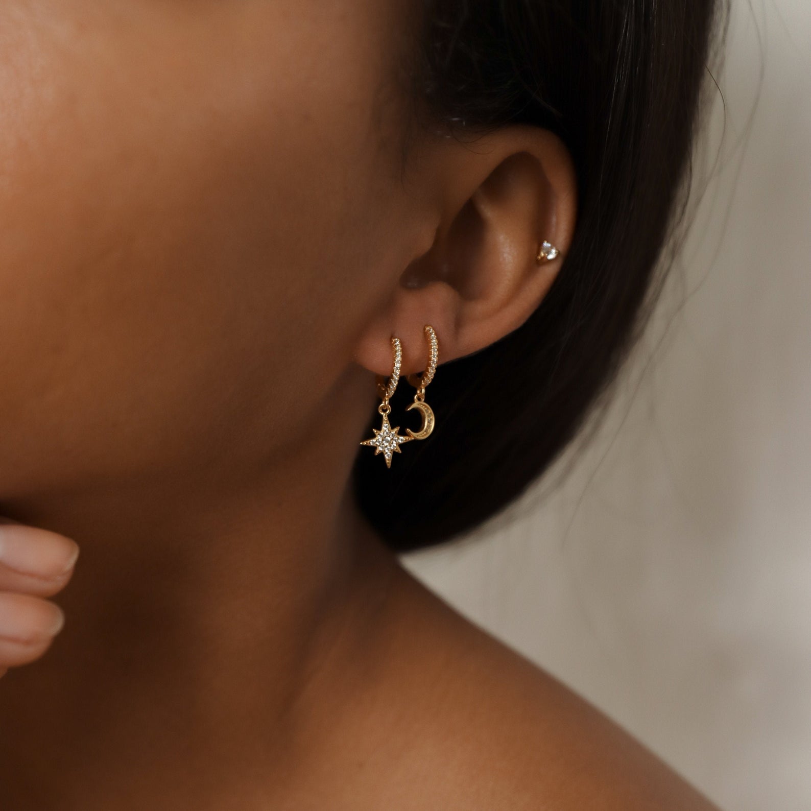 Close-up of a woman's ear wearing Moon and Star Huggies, along with constellation-inspired earrings—a stud and a delicate star charm hoop.