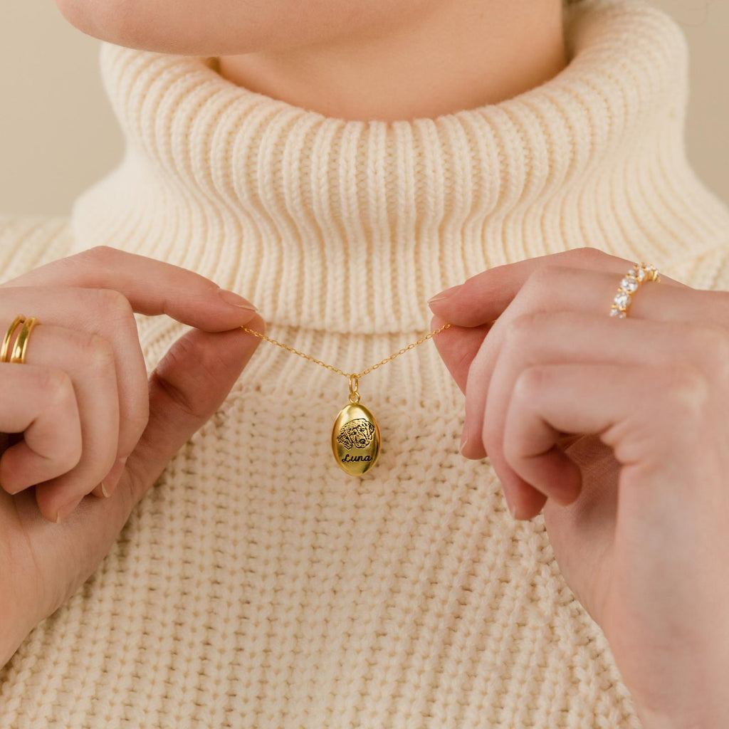 A person in a cream turtleneck holds an Oval Pet Necklace with both hands.