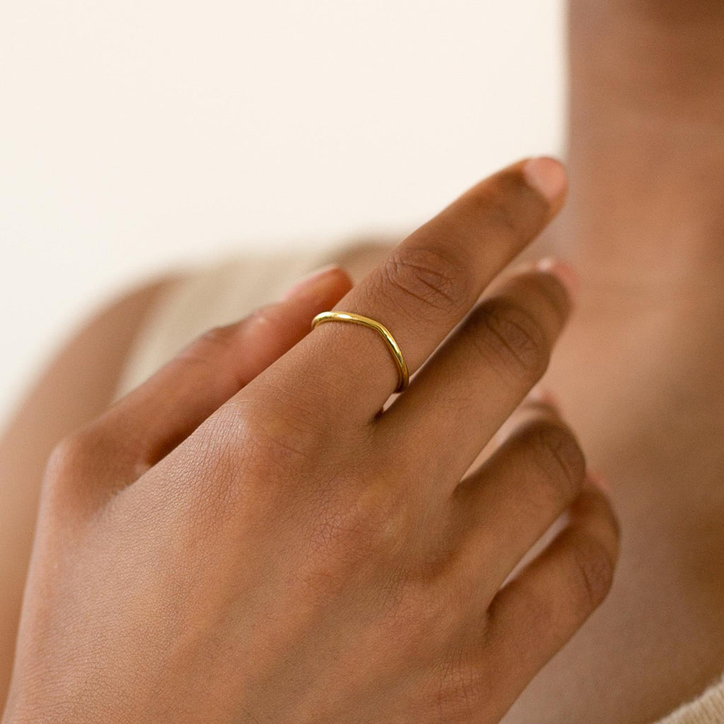 A hand wears the Dainty Wave Band, a modern minimalist ring, on the middle finger against a neutral background.