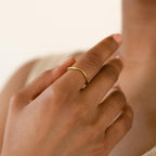 A hand wears the Dainty Wave Band, a modern minimalist ring, on the middle finger against a neutral background.