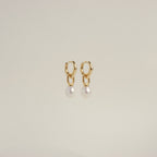 The Hazel Pearl Hoops are gold hoop earrings with dangling white pearls, a modern jewelry standout, elegantly showcased against a plain light background.
