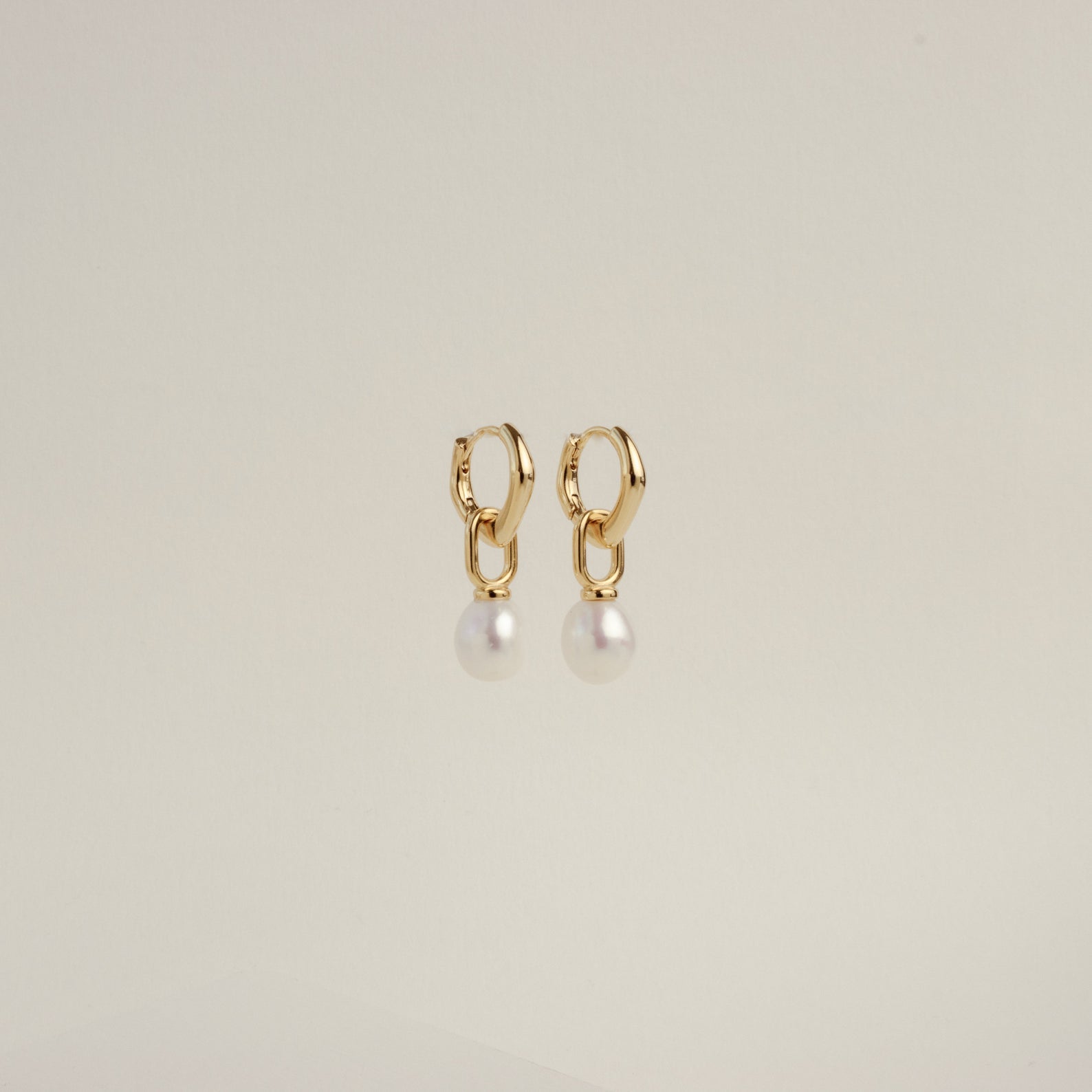 The Hazel Pearl Hoops are gold hoop earrings with dangling white pearls, a modern jewelry standout, elegantly showcased against a plain light background.