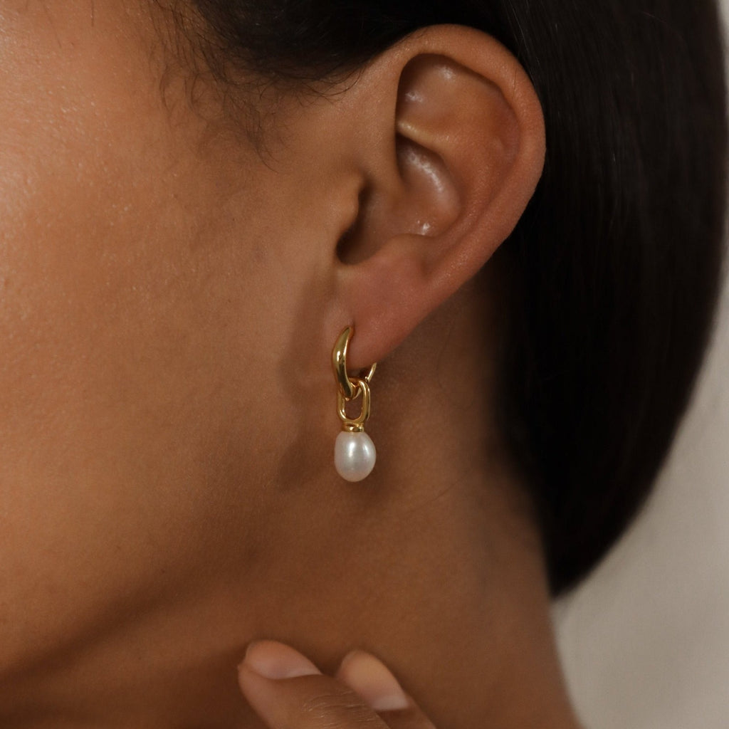 Close-up of an ear wearing our Hazel Pearl Hoops—gold hoop earrings with a hanging white pearl—ideal for lovers of modern jewelry.