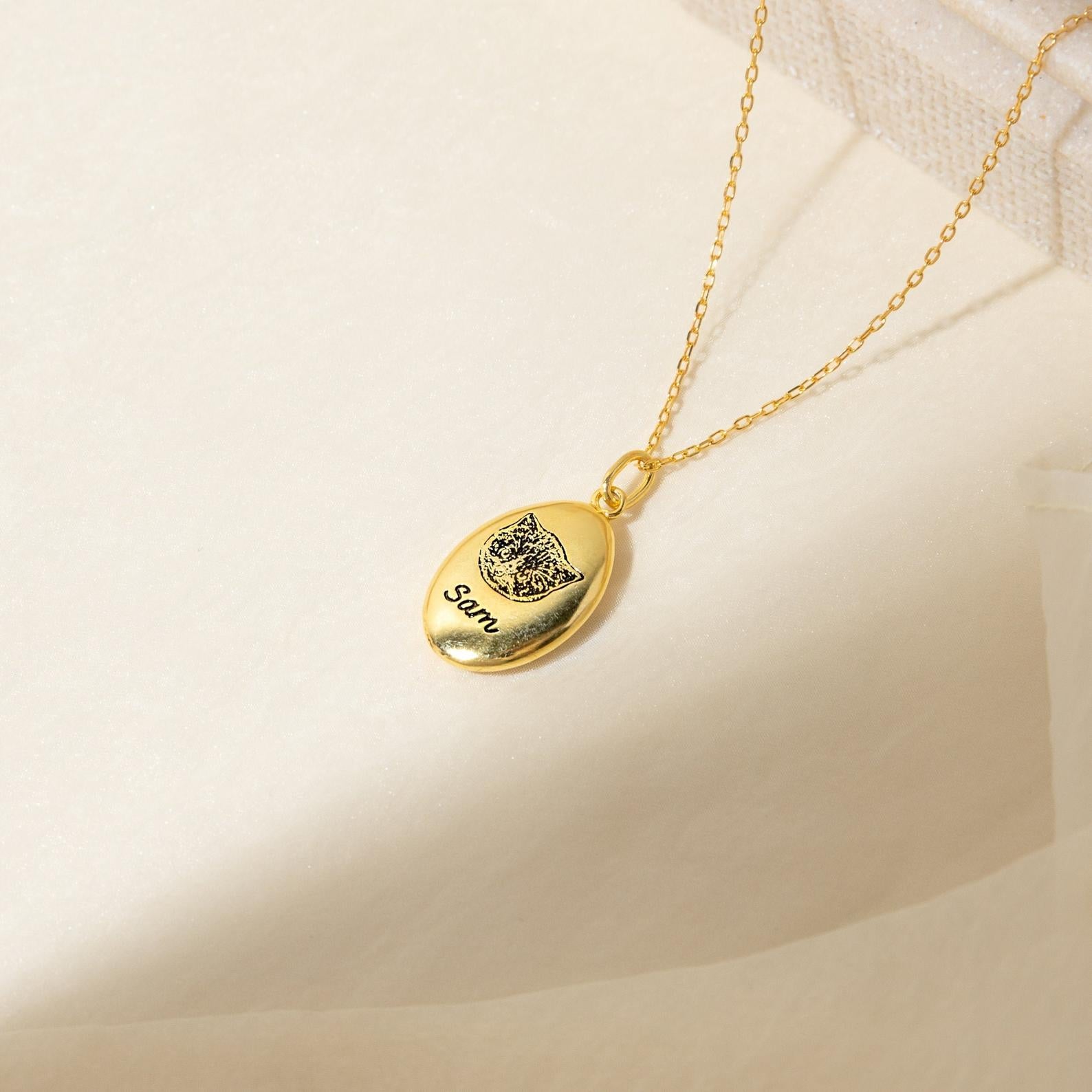 Oval Pet Necklace with an engraved cat face and the name Sam on a soft cream background—a charming personalized pet jewelry piece.