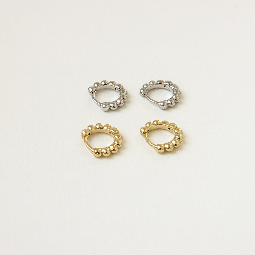 Two pairs of Dainty Sphere Beaded Huggies—one in silver, one in gold—are displayed on a light beige background.