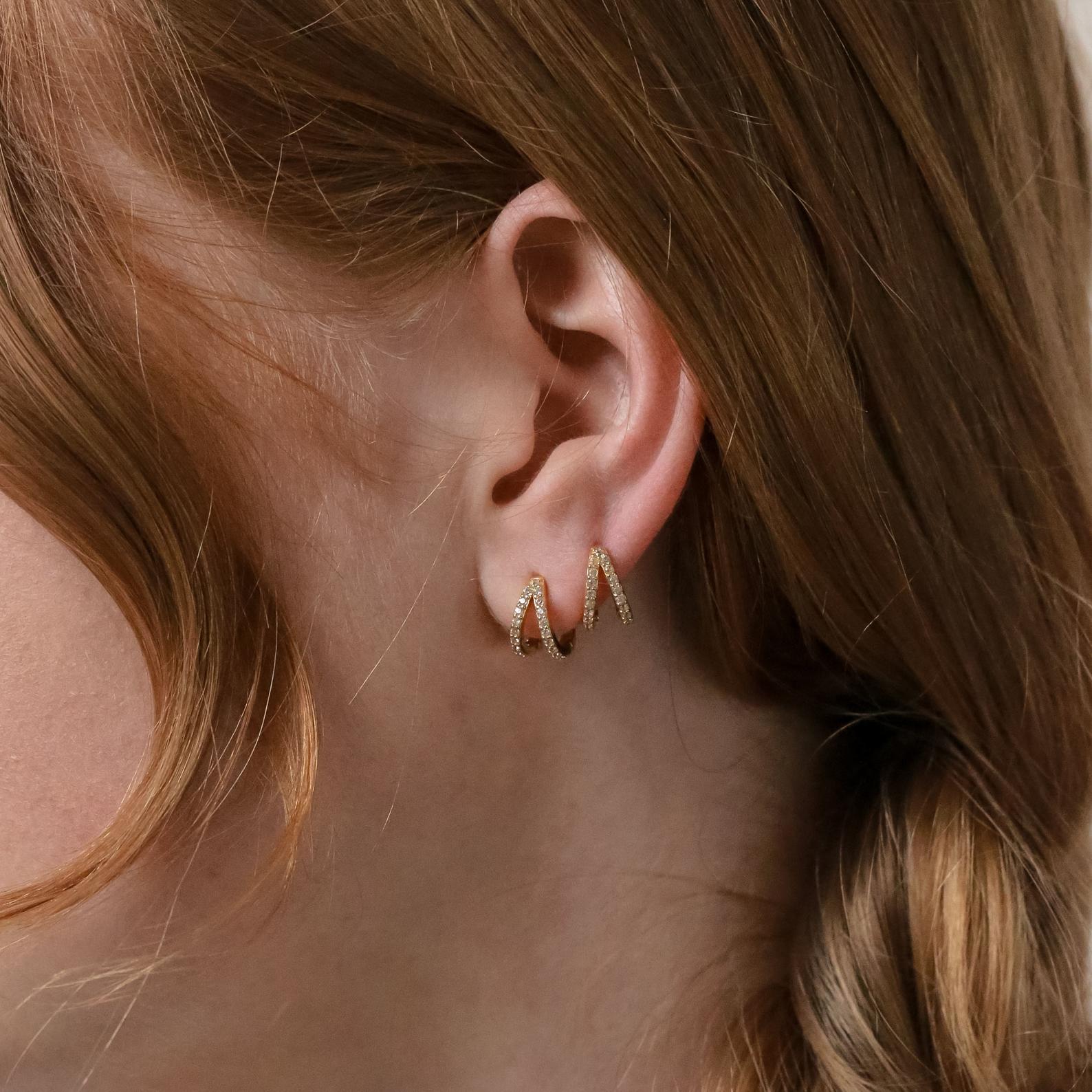 Close-up of a woman's ear wearing Esther Duo Pave Huggies, featuring two gold arches—one with sparkling pavé detail for extra shine.