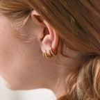 Close-up of a person's ear wearing the Esther Duo Pave Huggies—one hoop with braided details, the other with sparkling pave—for a stunning multi-textured look.