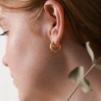 Close-up of a woman's ear wearing the Morgan Croissant Hoops, capturing the French girl aesthetic with part of her face and hair visible—modern gold earrings designed for effortless style.