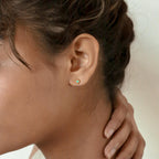 A woman's hand gently touches her neck, showcasing the delicate Mara Studs in her ear.