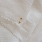 Two Mara Studs, featuring gold and a hint of turquoise, are displayed elegantly on a white cloth.