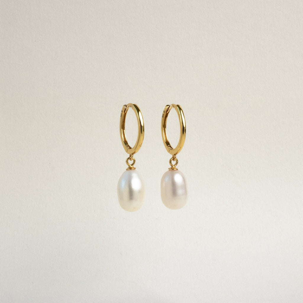 The Maggie Pearl Drop Hoops are gold modern earrings with dangling oval white pearls, displayed against a plain light background—ideal for minimal jewelry lovers.