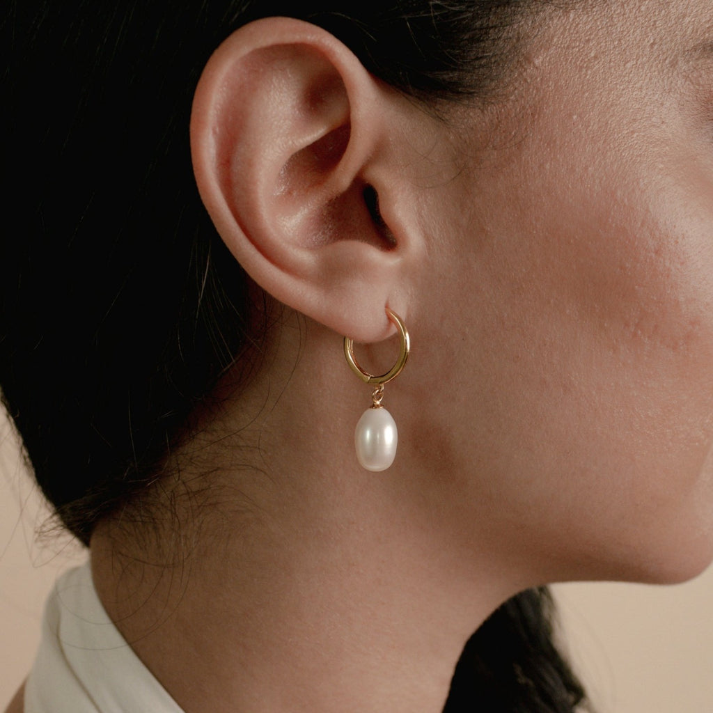 Close-up of a woman's ear wearing Maggie Pearl Drop Hoops—modern gold hoops with a dangling white pearl, perfect for minimal jewelry lovers.