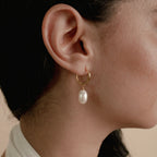 Close-up of a woman's ear wearing Maggie Pearl Drop Hoops—modern gold hoops with a dangling white pearl, perfect for minimal jewelry lovers.