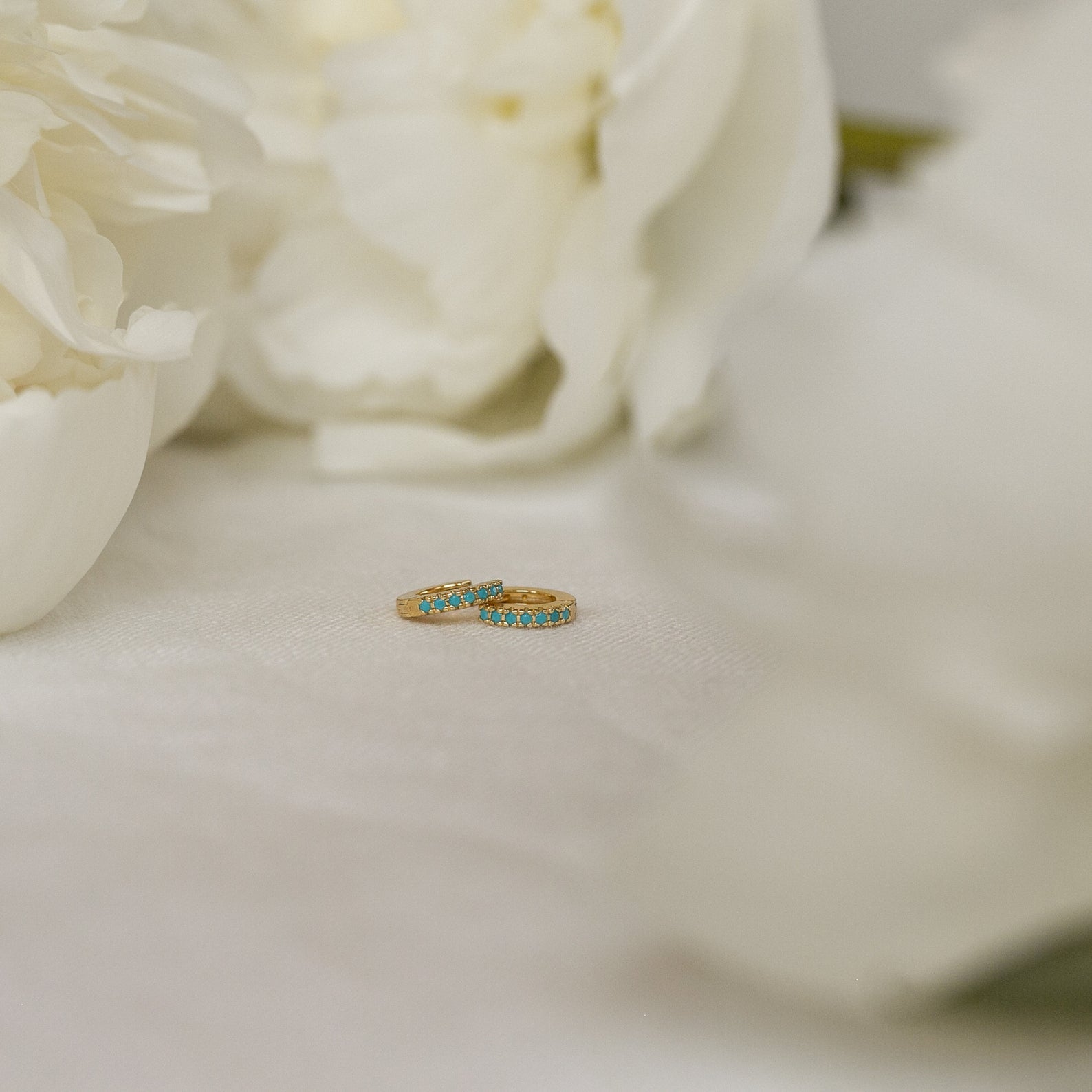 The Kendra Huggies feature gold rings with blue stones, exuding eclectic charm—ideal for stacking or pairing with your favorite turquoise jewelry on a white surface.