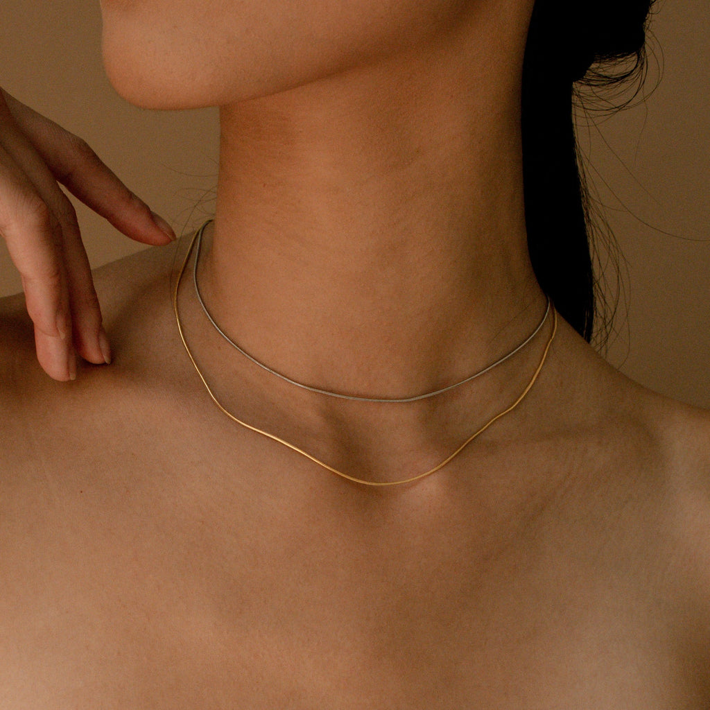 The gold and white gold snake chains worn together as a layered choker look on a model