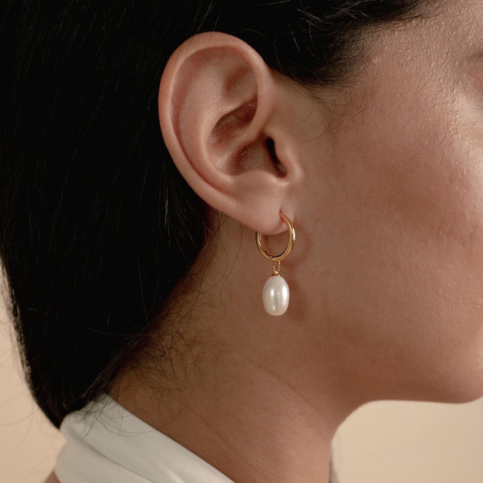 Close-up of a woman's ear wearing the Maggie Pearl Drop Hoops—minimal gold hoops featuring a dangling white pearl.