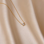 The Dainty Diamond Necklace, featuring a single small diamond charm, is displayed on smooth light beige satin fabric for a soft and elegant presentation.