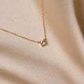 The Dainty Diamond Necklace, featuring a single small diamond charm on a delicate 925 sterling silver chain, is displayed on smooth light beige satin fabric for an elegant touch.