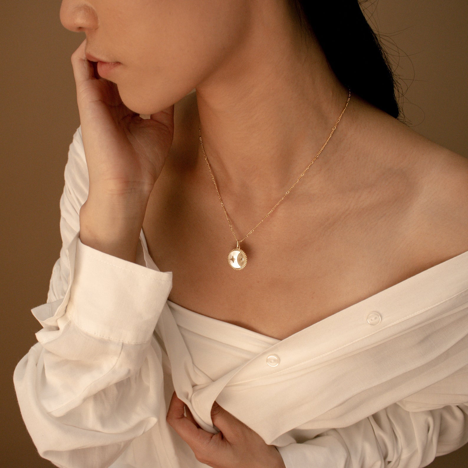 A woman wearing a white off-shoulder shirt models the Gabi Coin Necklace with minimal jewelry against a beige background.