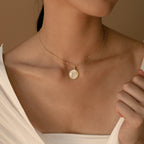 A woman is shown from shoulders to chin wearing a white top and the Gabi Coin Necklace, a minimal gold necklace featuring a round pendant.