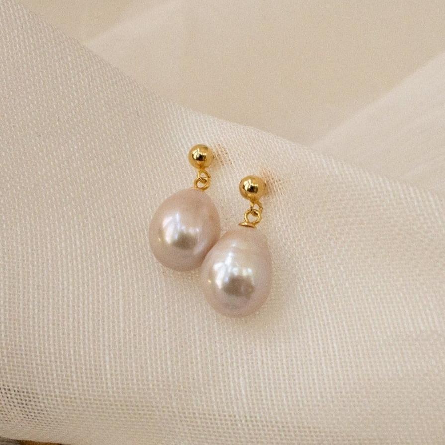 Baroque Pearl Earrings with gold studs and white pearls add a classic touch, making them perfect statement earrings against a soft, cream-colored fabric background.