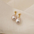 Baroque Pearl Earrings with gold studs and white pearls add a classic touch, making them perfect statement earrings against a soft, cream-colored fabric background.