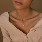 A woman wears a light beige blouse with the Laura Starburst Duo Necklace in 18K Gold, featuring a delicate pendant and a starburst charm on layered chains.