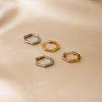 Two pairs of Parker Pave Hexagon Huggies—one silver, one gold—featuring small crystals for sparkle, displayed on beige fabric. A chic ear accessory.