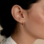 Close-up of a woman's ear wearing Parker Pave Hexagon Huggies, the small gold earrings sparkling with embedded gemstones.