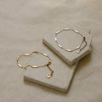 The Abby Bar Link Bracelet is shown in gold and 925 sterling silver on light stone slabs over textured beige fabric, each with a delicate chain and a small heart charm.