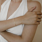 A person wearing a sleeveless white top crosses their arms, showcasing the delicate Abby Bar Link Bracelet on their wrist.