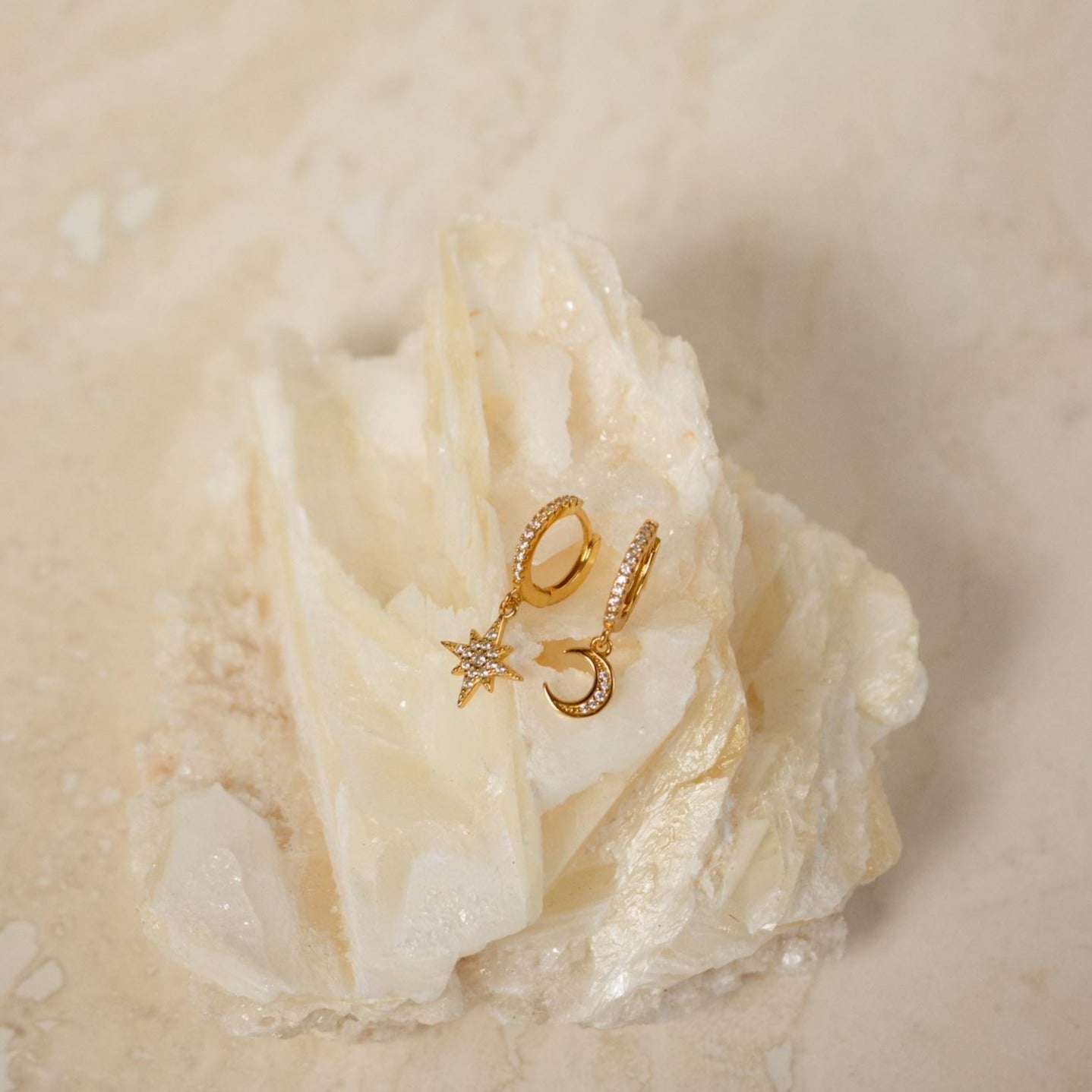 Moon and Star Huggies in Sterling Silver, featuring star and crescent moon charms, are showcased on a creamy, textured stone surface.