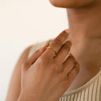 A person touches their neck while wearing the Dainty Wave Band and a beige ribbed top.