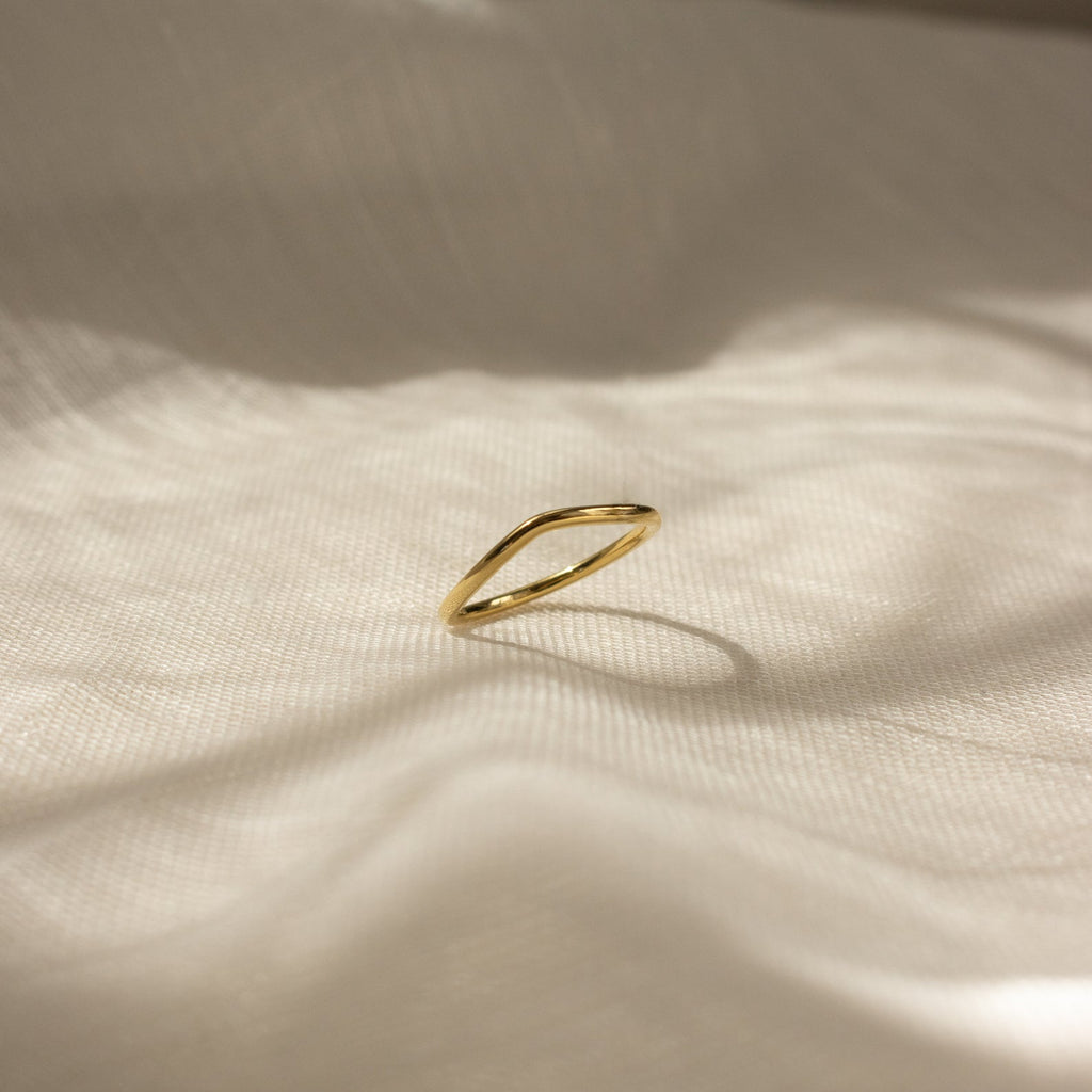 The Dainty Wave Band, a simple and contemporary ring, rests on softly textured cream-colored fabric in gentle sunlight and shadows.