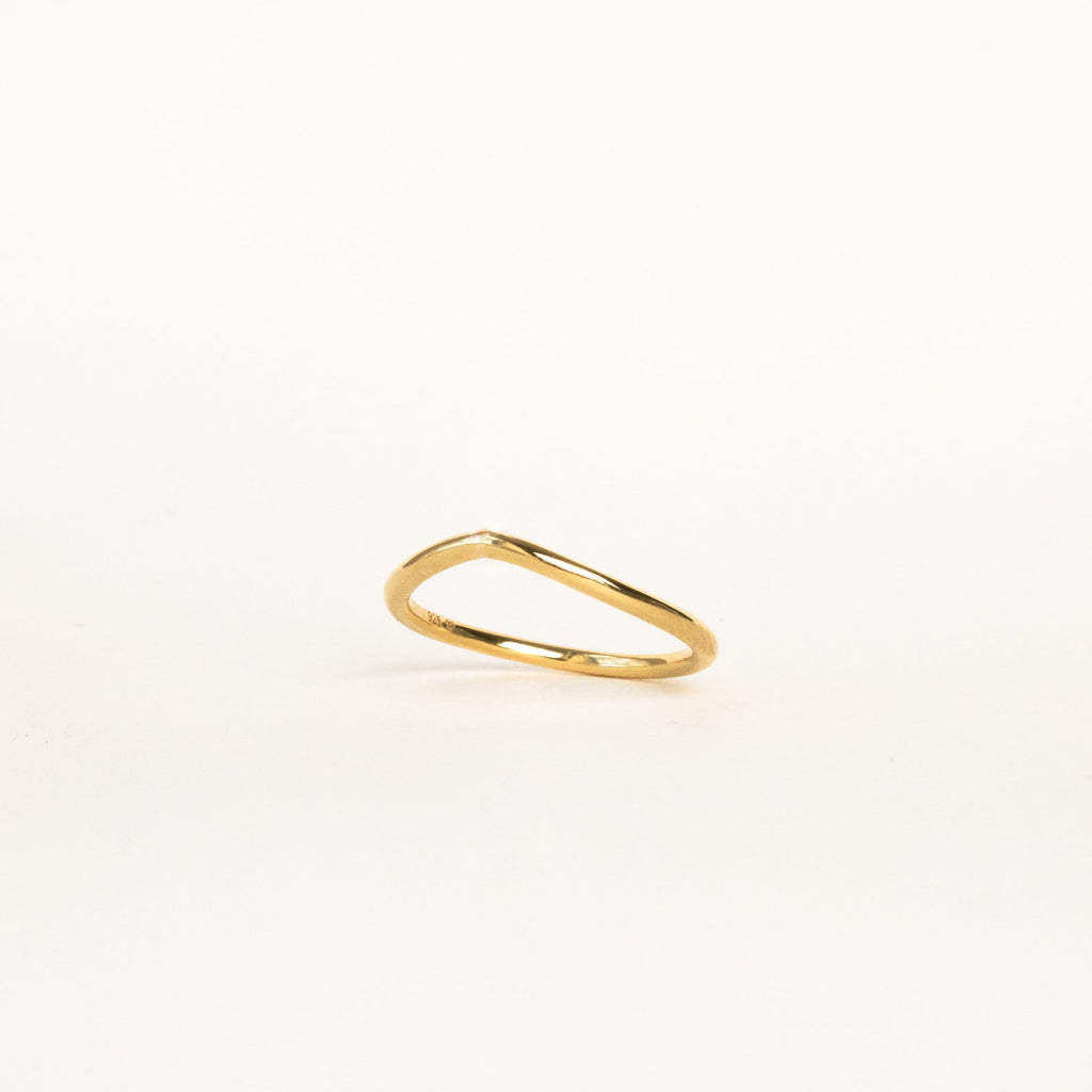 The Dainty Wave Band features a thin, elegant gold band with a delicate, slightly curved design, shown on a plain white background—an exquisite piece of modern jewelry.