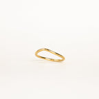 The Dainty Wave Band features a thin, elegant gold band with a delicate, slightly curved design, shown on a plain white background—an exquisite piece of modern jewelry.