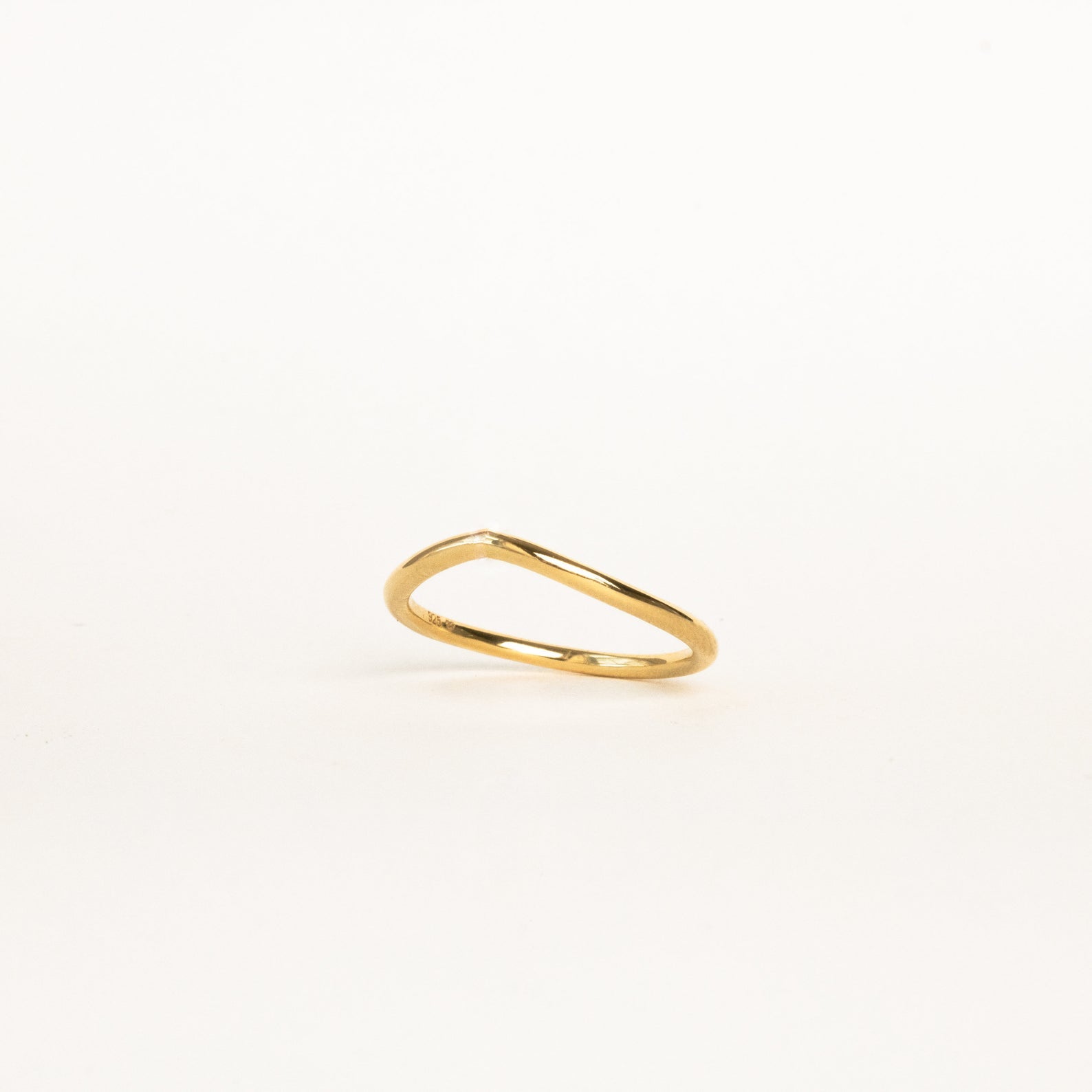 The Dainty Wave Band features a thin, elegant gold band with a delicate, slightly curved design, shown on a plain white background—an exquisite piece of modern jewelry.