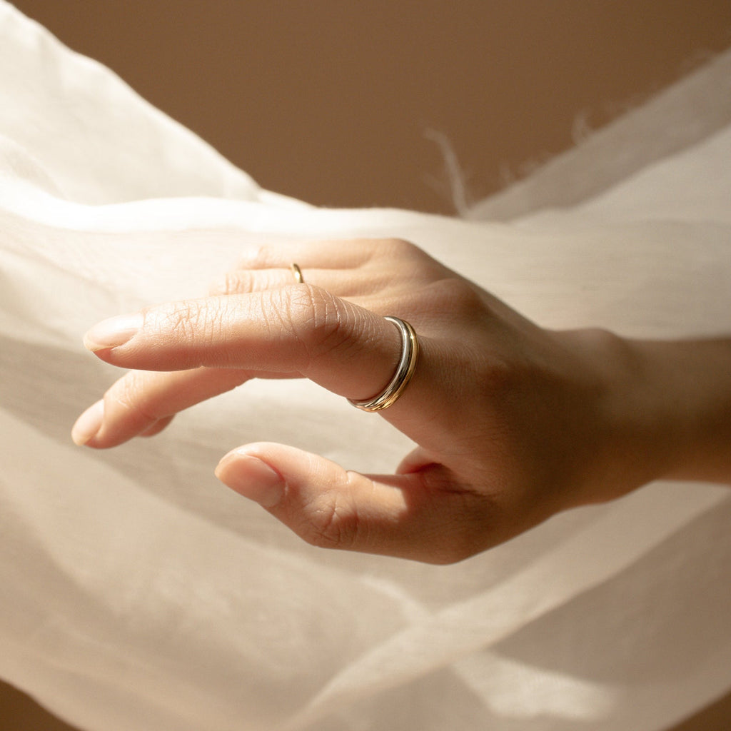 A hand wearing the Minimal Stacking Ring gently reaches toward sheer white fabric, illuminated by soft lighting.