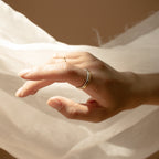 A hand wearing the Minimal Stacking Ring gently reaches toward sheer white fabric, illuminated by soft lighting.