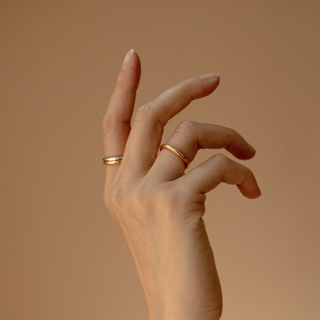 A hand adorned with a Minimal Stacking Ring is gracefully posed against a neutral beige background.