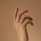 A hand adorned with a Minimal Stacking Ring is gracefully posed against a neutral beige background.