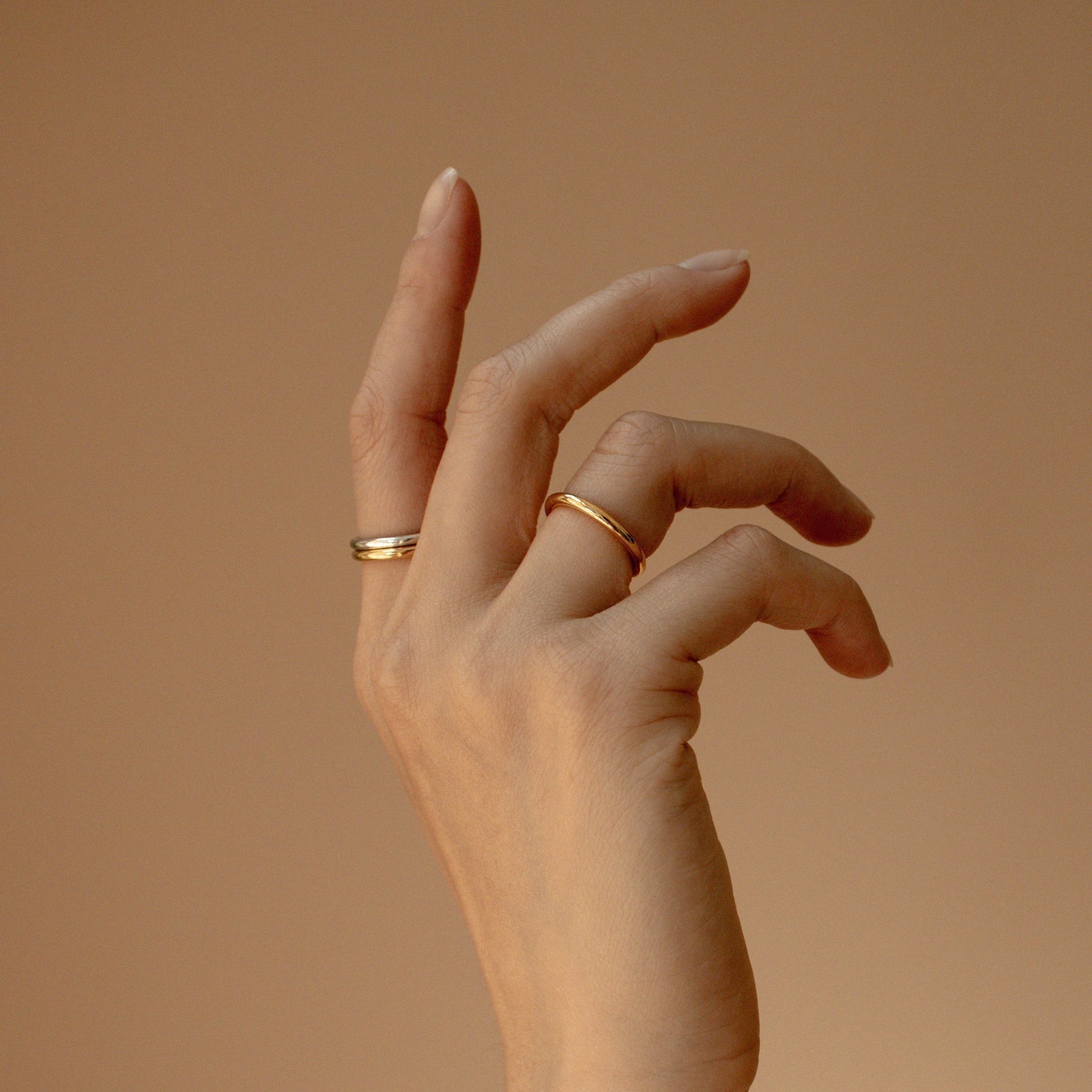 A hand adorned with a Minimal Stacking Ring is gracefully posed against a neutral beige background.