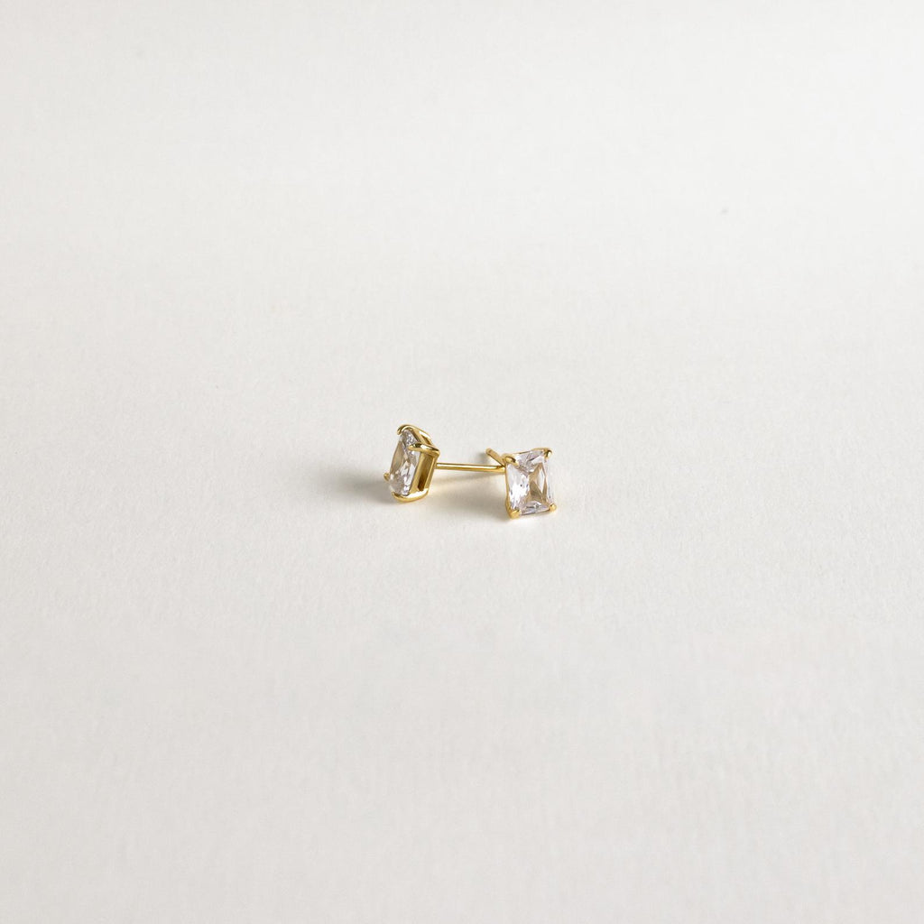 Emerald Diamond Studs—classic gold prong-set earrings featuring rectangular clear stones that sparkle elegantly against a plain white background.
