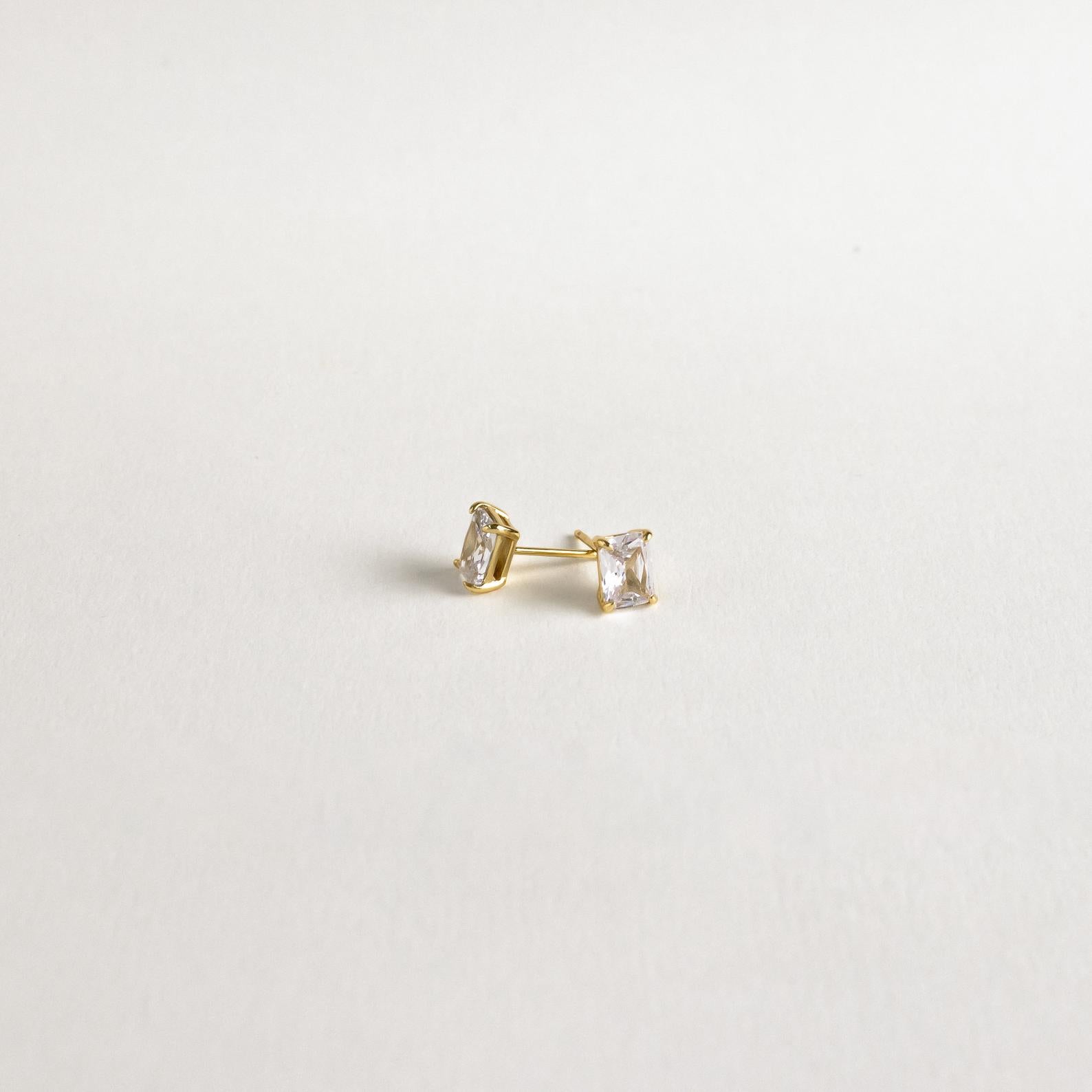 Emerald Diamond Studs—classic gold prong-set earrings featuring rectangular clear stones that sparkle elegantly against a plain white background.