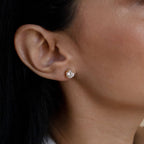 Close-up of a woman's ear wearing Round Diamond Studs—classic gold stud earrings featuring a round, clear gemstone, showcasing elegant solitaire diamond jewelry.