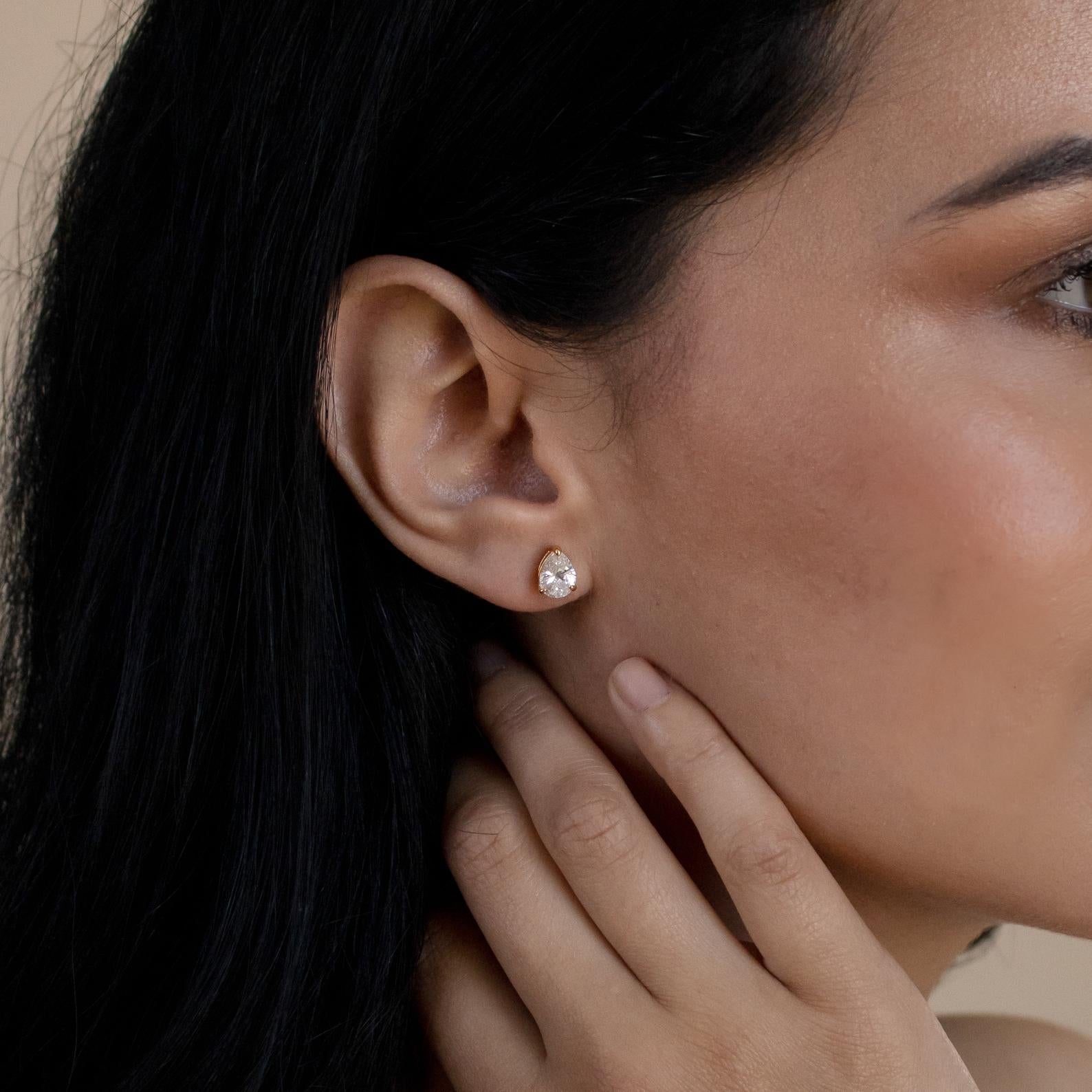 Close-up of a woman's ear with a hand on her neck, wearing Pear Diamond Studs—minimalistic earrings that add a touch of sparkle.