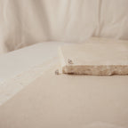 The Pear Diamond Studs, featuring two small, pear-shaped diamonds, rest on a textured beige stone surface with a neutral backdrop—an ideal choice for lovers of minimalistic earrings.