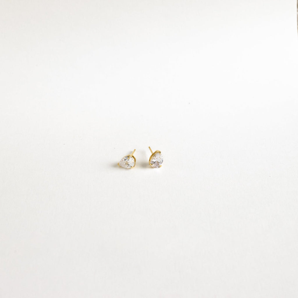 Pear Diamond Studs: Minimalistic gold earrings with small, heart-shaped clear stones, elegantly showcased on a plain white background.
