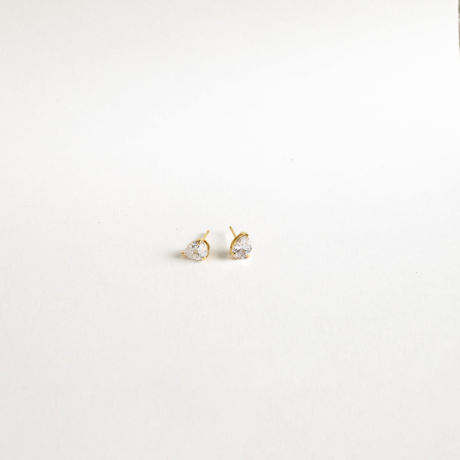 Pear Diamond Studs: Minimalistic gold earrings with small, heart-shaped clear stones, elegantly showcased on a plain white background.