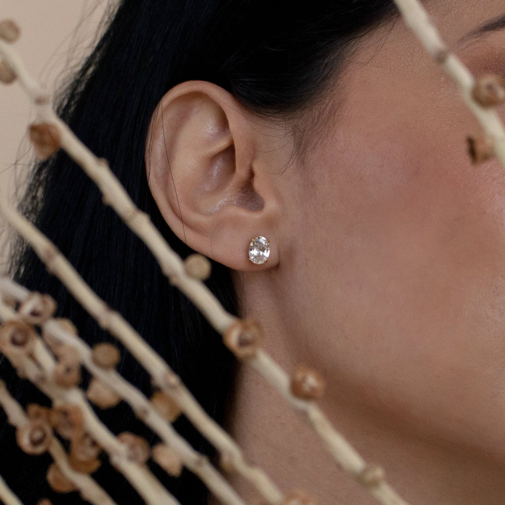Close-up of a woman's ear wearing Oval Diamond Studs, with dried plant stems in the foreground.